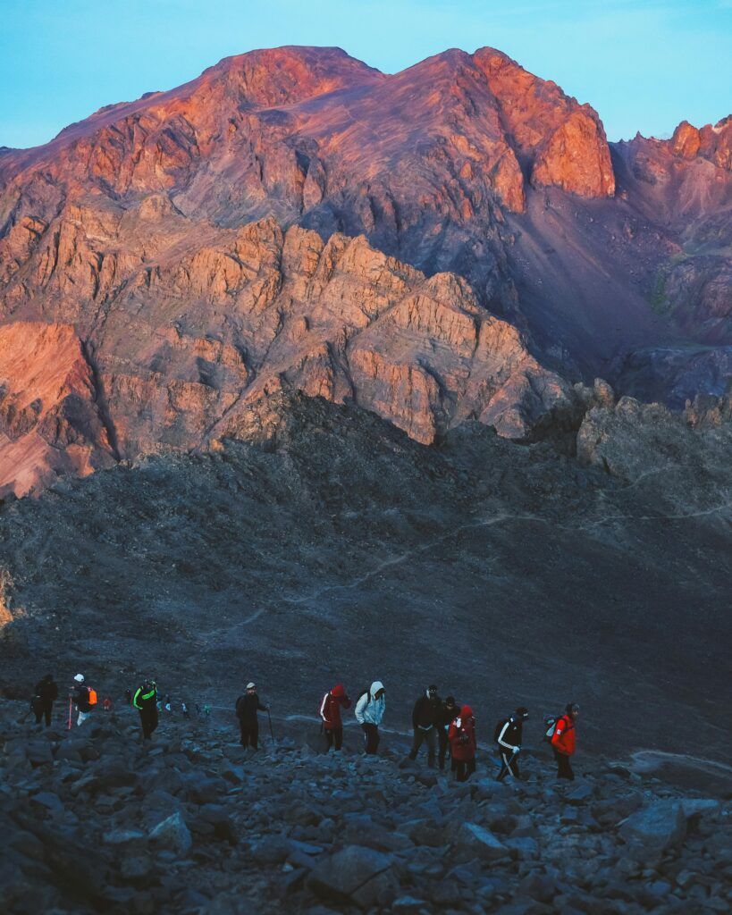 Experiencia de senderismo en el Alto Atlas A group of hikers walking through rocky terrain in the scenic Al-Aroui mountains at dusk.